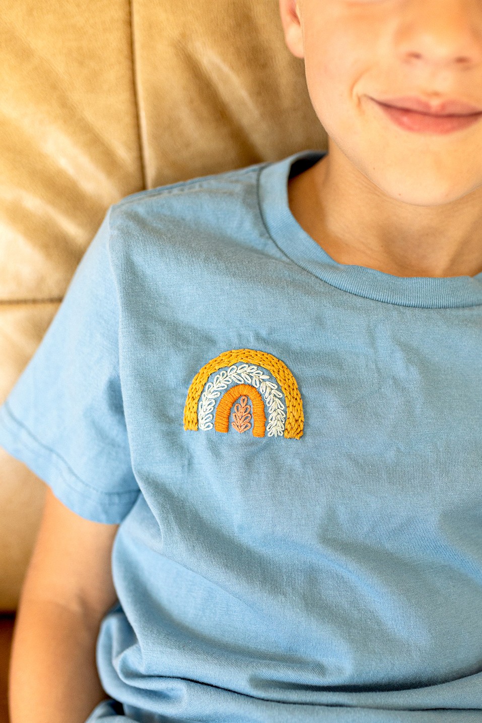 A little boy smiles, wearing a shirt with a rainbow embroidered on it.