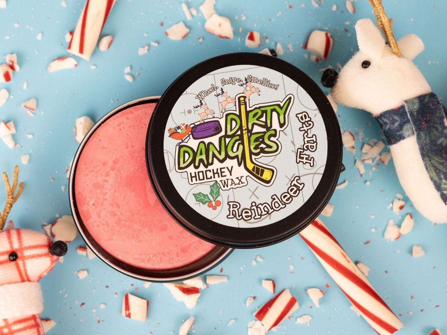 A tin of dirty dangles reindeer farts holiday hockey stick wax on a blue background with candy canes and reindeer