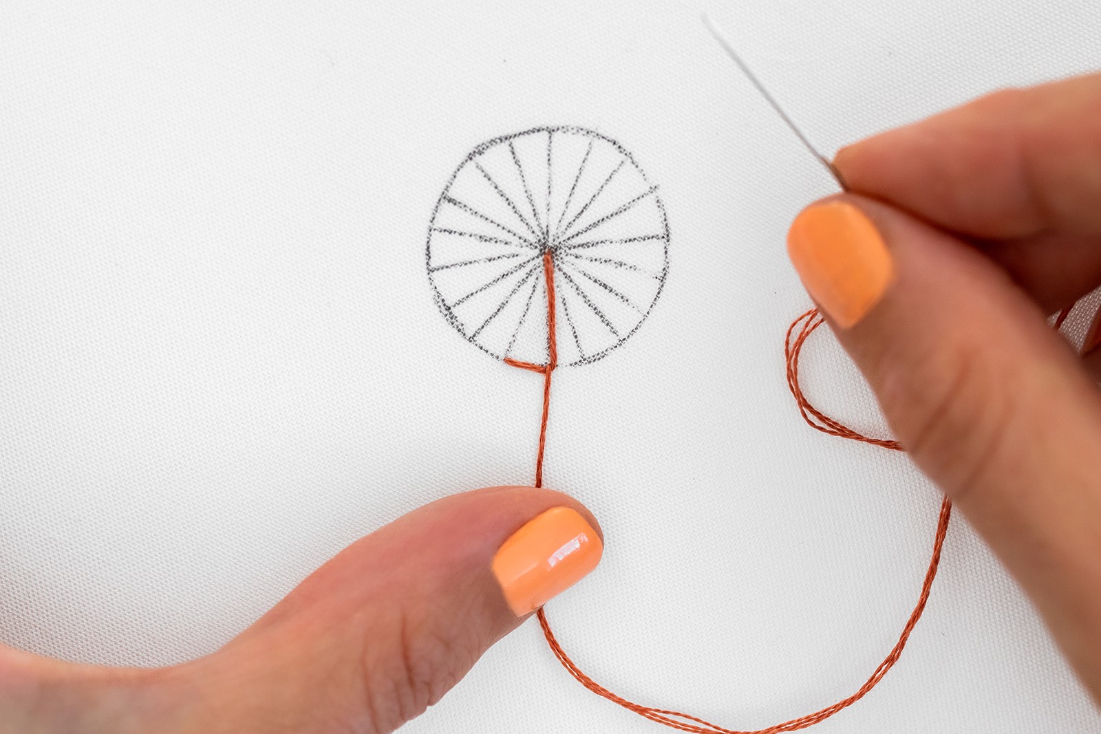 A hand presses a thread down on a button wheel shape.