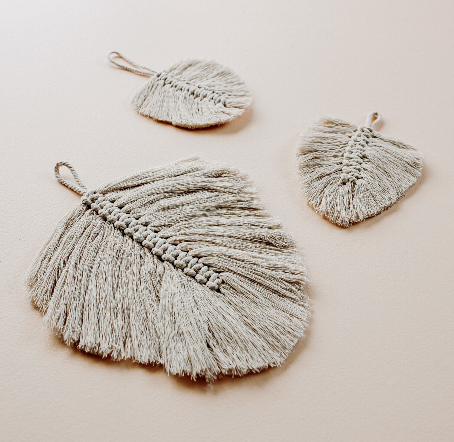 A large macrame leaf and two small macrame leaves lay on a table.
