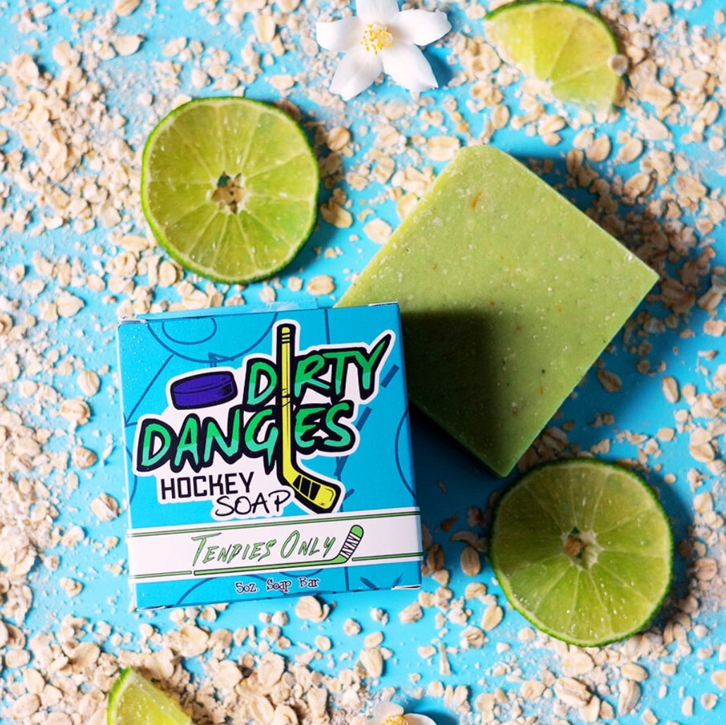 A green bar of dirty dangles hockey soap on a blue background with oats and limes