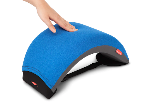 A hand pressing the surface of a blue nap pillow with an arc design to prevent poor sleep in an office setting.