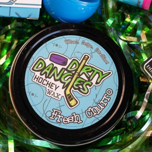 A tin of dirty dangles hockey wax fresh churro scent in an easter basket with green easter grass
