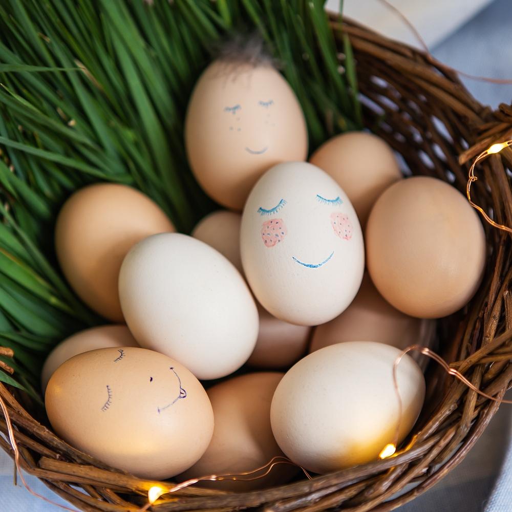 eggs with a cute face that lie in a wooden basket decorated with warm lights.