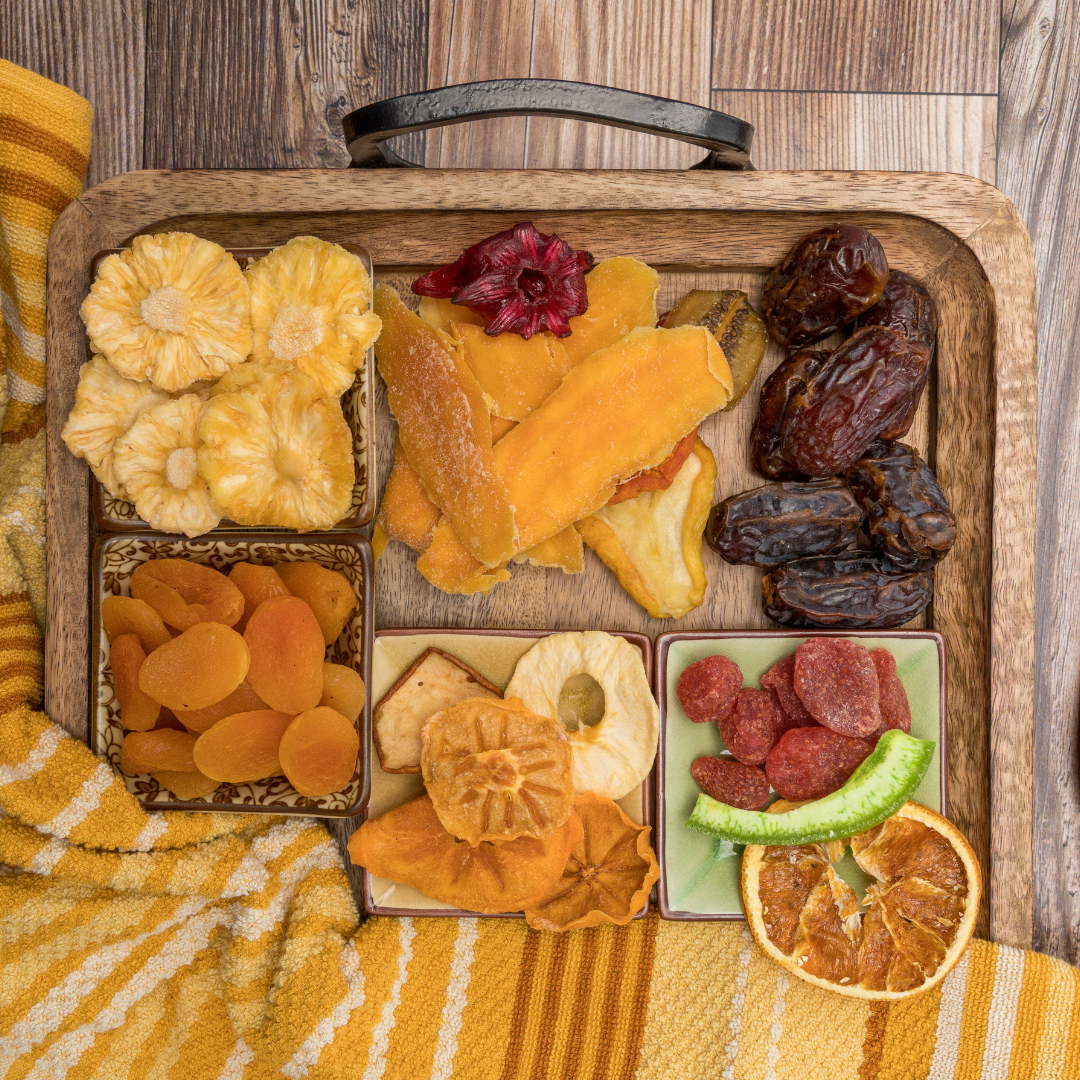 A wooden tray filled with an assortment of colorful dried fruits, including apricots, apples, pineapple, and dates, neatly arranged with a cozy fabric underneath.