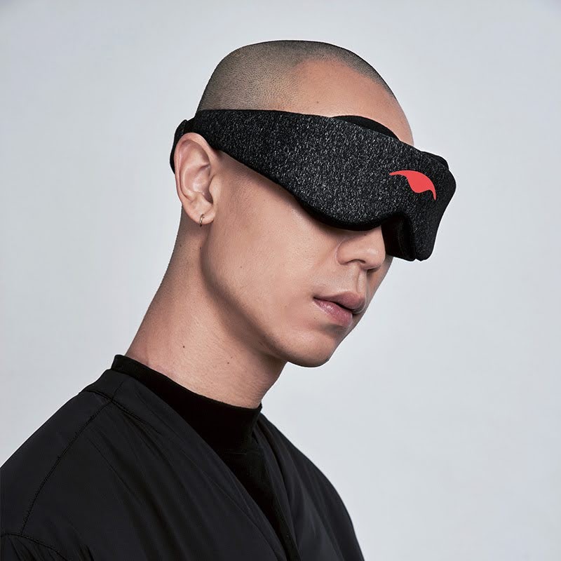 A bald man wearing a black sleep mask with eye cups.