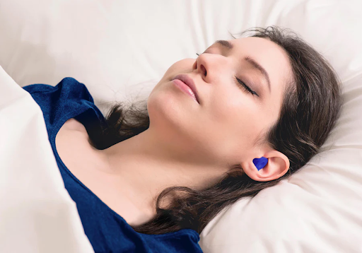 A sleeping girl lying in bed wearing blue earplugs.
