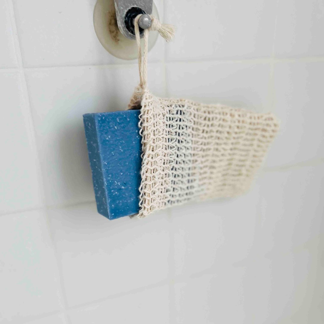 A tan soap bag hanging in a white tile shower