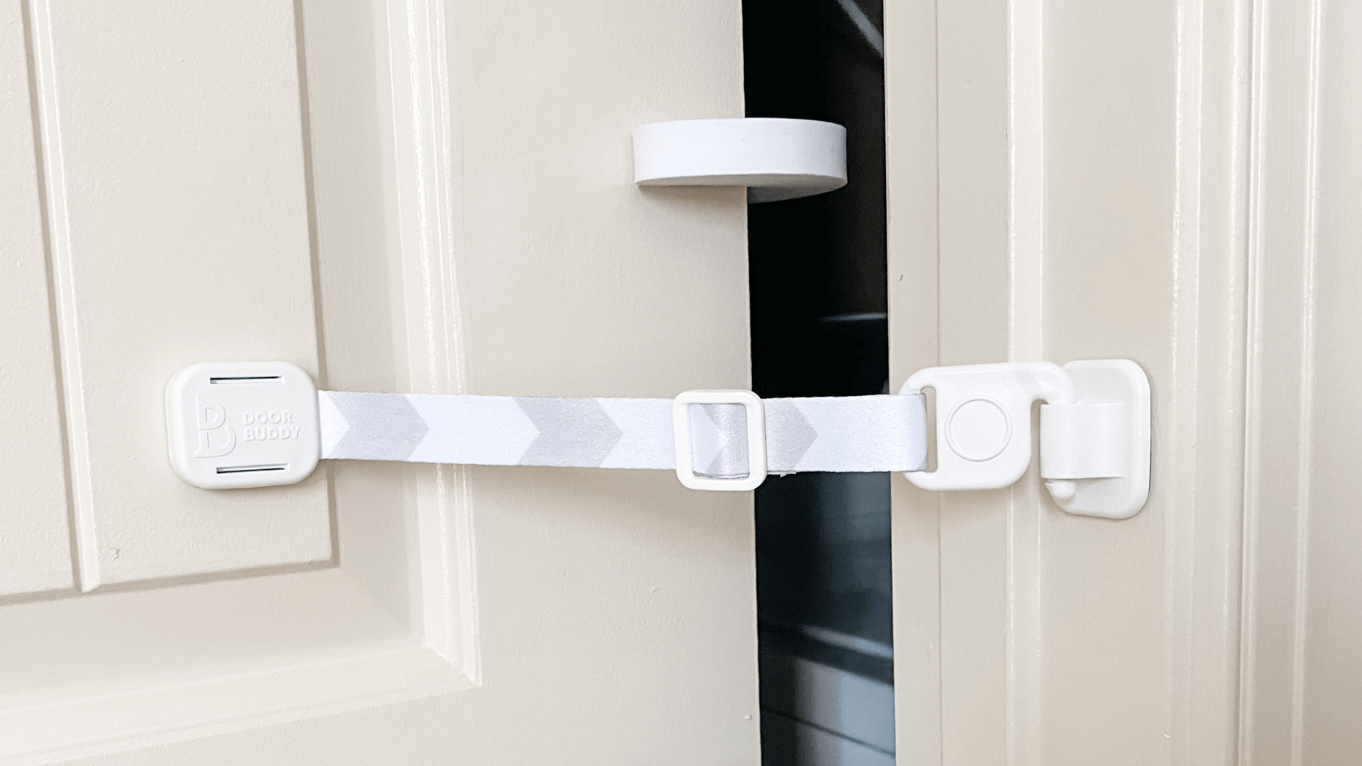 The Door Buddy adjustable door strap and door stopper installed on a door to hold it slightly open. This baby proofing solution creates a small gap for cats to pass through while helping keep babies toddlers and dogs out of the room.