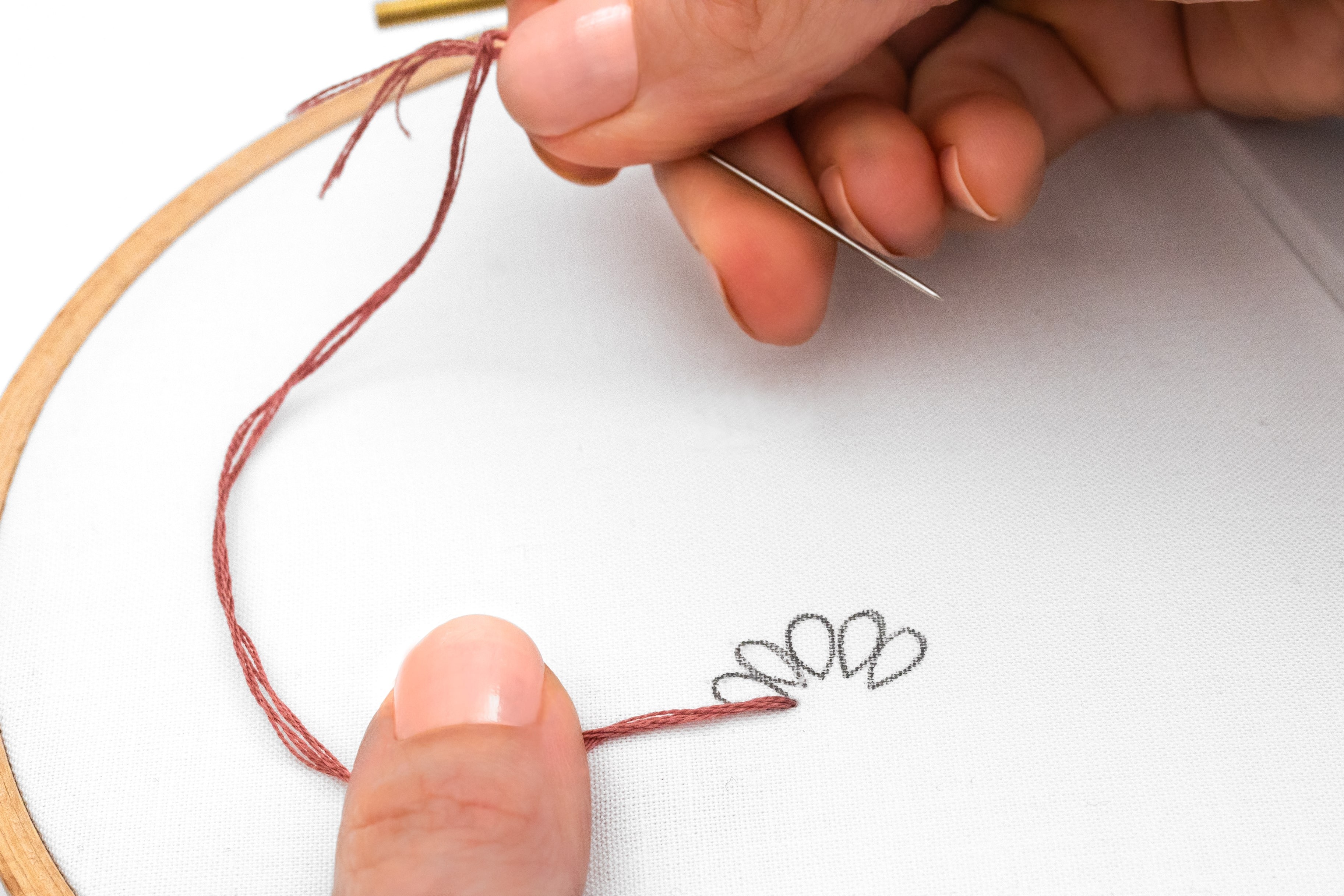 A hand holds a piece of thread over a petal shape.