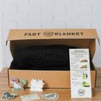 A black dutch oven kits blanket in a box with a recipe card and stickers on a wood background