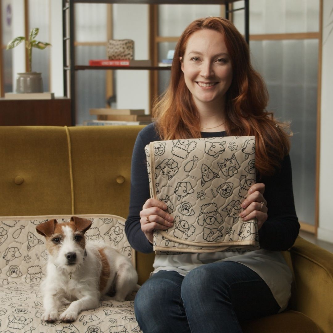 Woman sitting on sofa next to terrier dog, holding reusable potty pad