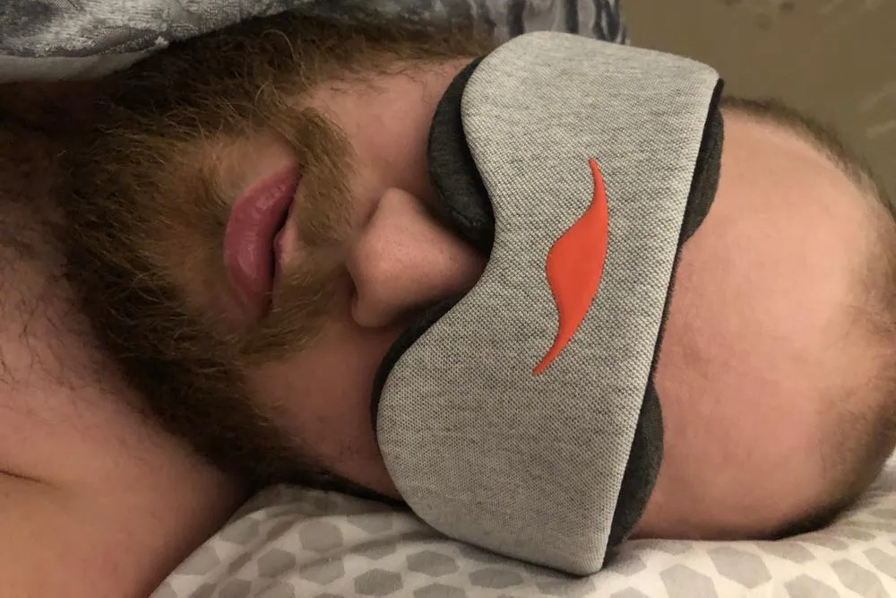 A man lying down on his side wearing an eye mask with dark gray eye cups.