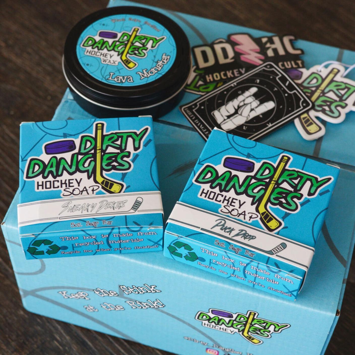 Assorted Dirty Dangles hockey products on a wood table with a blue dirty dangles subscription box.