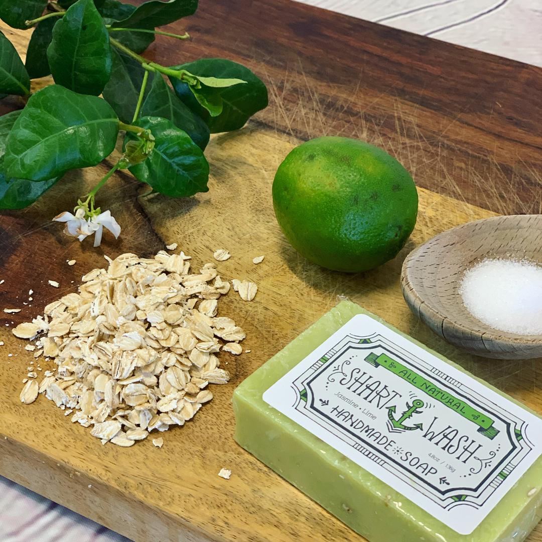 picture of a green and white jasmine flower, oatmeal, lime, sea salt and a bar of jasmine lime shart wash soap on a wood background