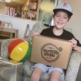 A kid smiling while holding a dutch oven kits gift box