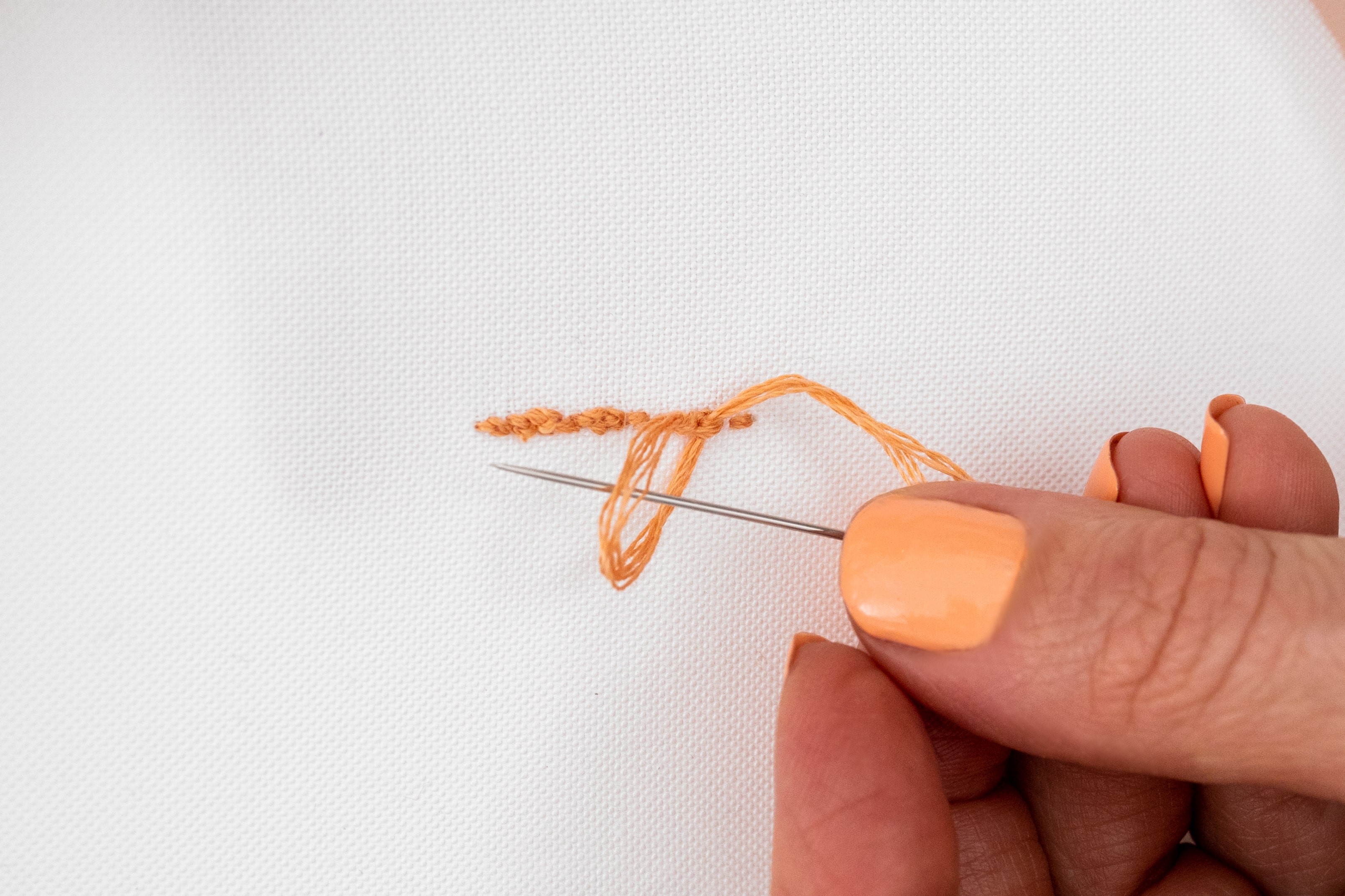 A needle is threaded under a tail of thread under the backside of the hoop - tidying the tail.