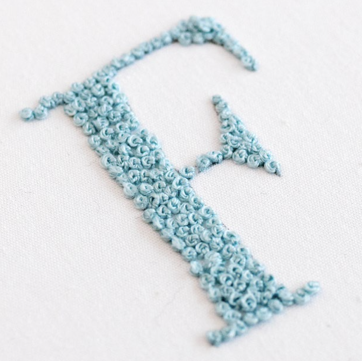 The letter F is stitched using french knots.