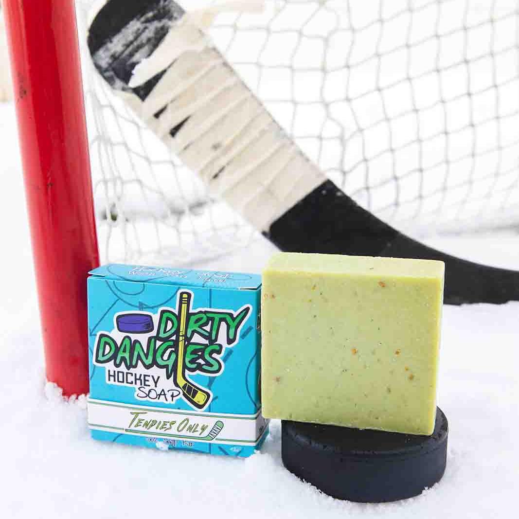 A black soap bar sits in the snow with a hockey goal, hockey puck and a hockey stick. Puck Drop