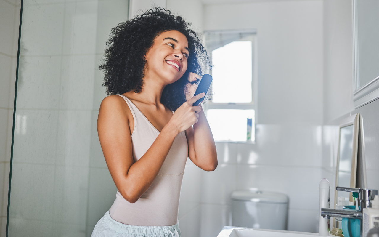 woman brushing her natural hair with a clean brush to fix an oily scalp