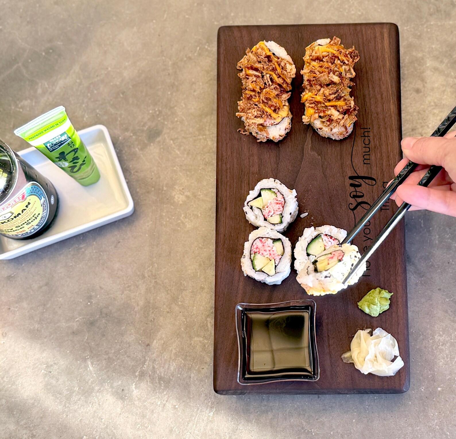 Single walnut wooden susho board with a hand holding a pair of chopsticks picking up a piece of sushi.