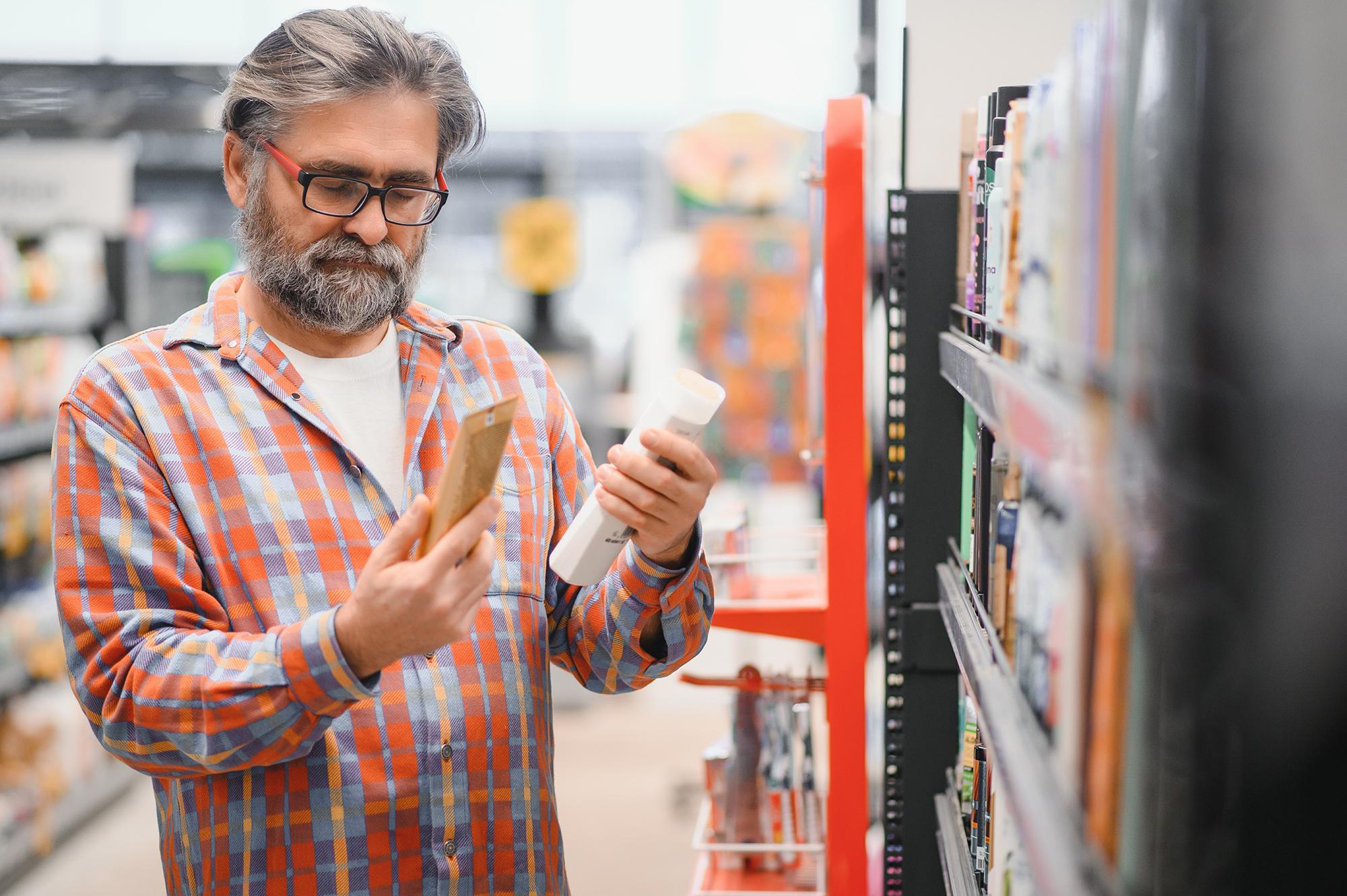 Man looking at multiple shampoo bottles on a store shelf, appearing uncertain about which product to choose.