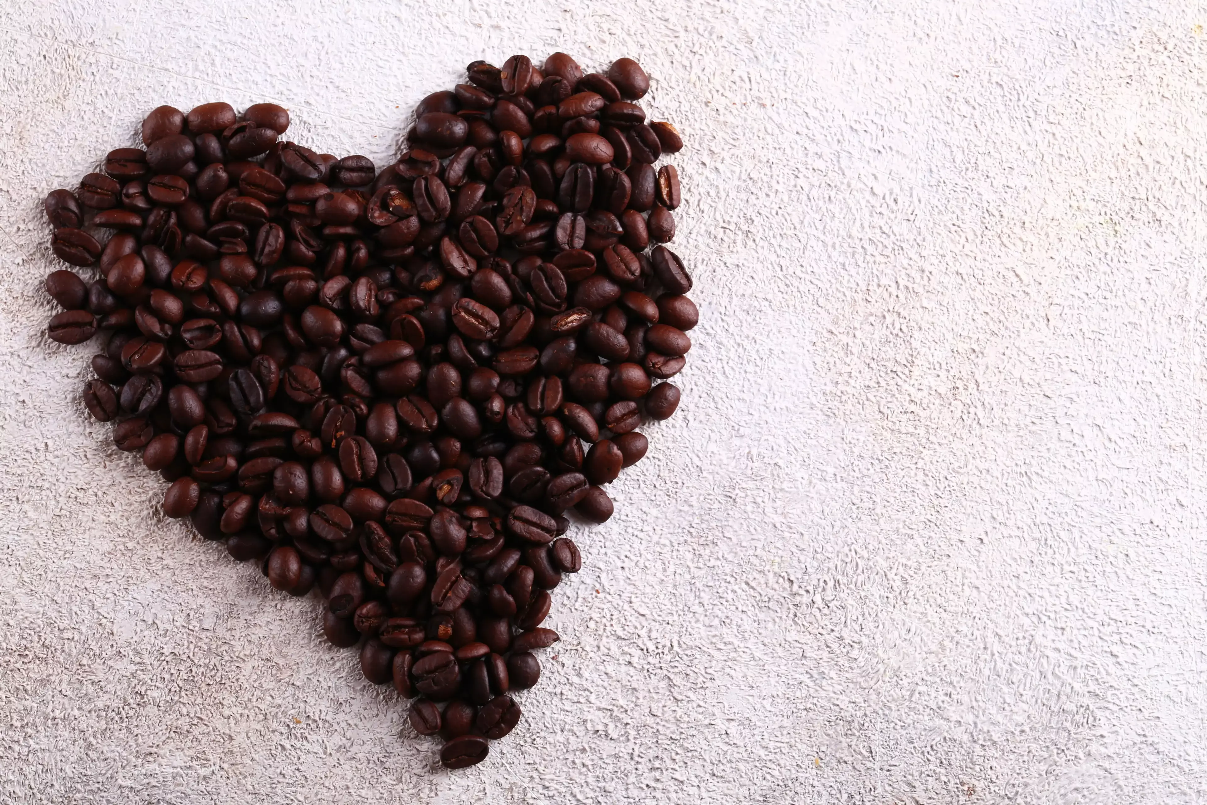 Heart-shaped arrangement of roasted coffee beans on a textured light background.