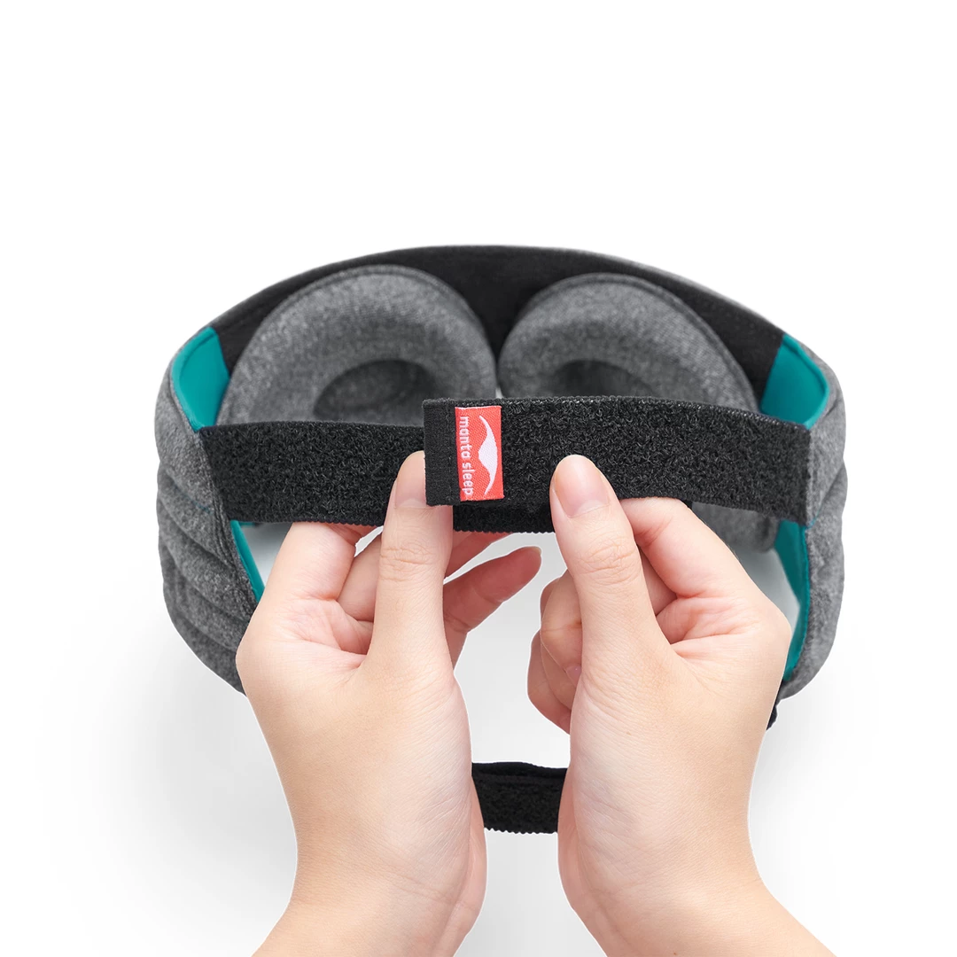 The back portion of a therapeutic sleep mask’s weighted head strap. Hands are demonstrating how the dup-strap design works.