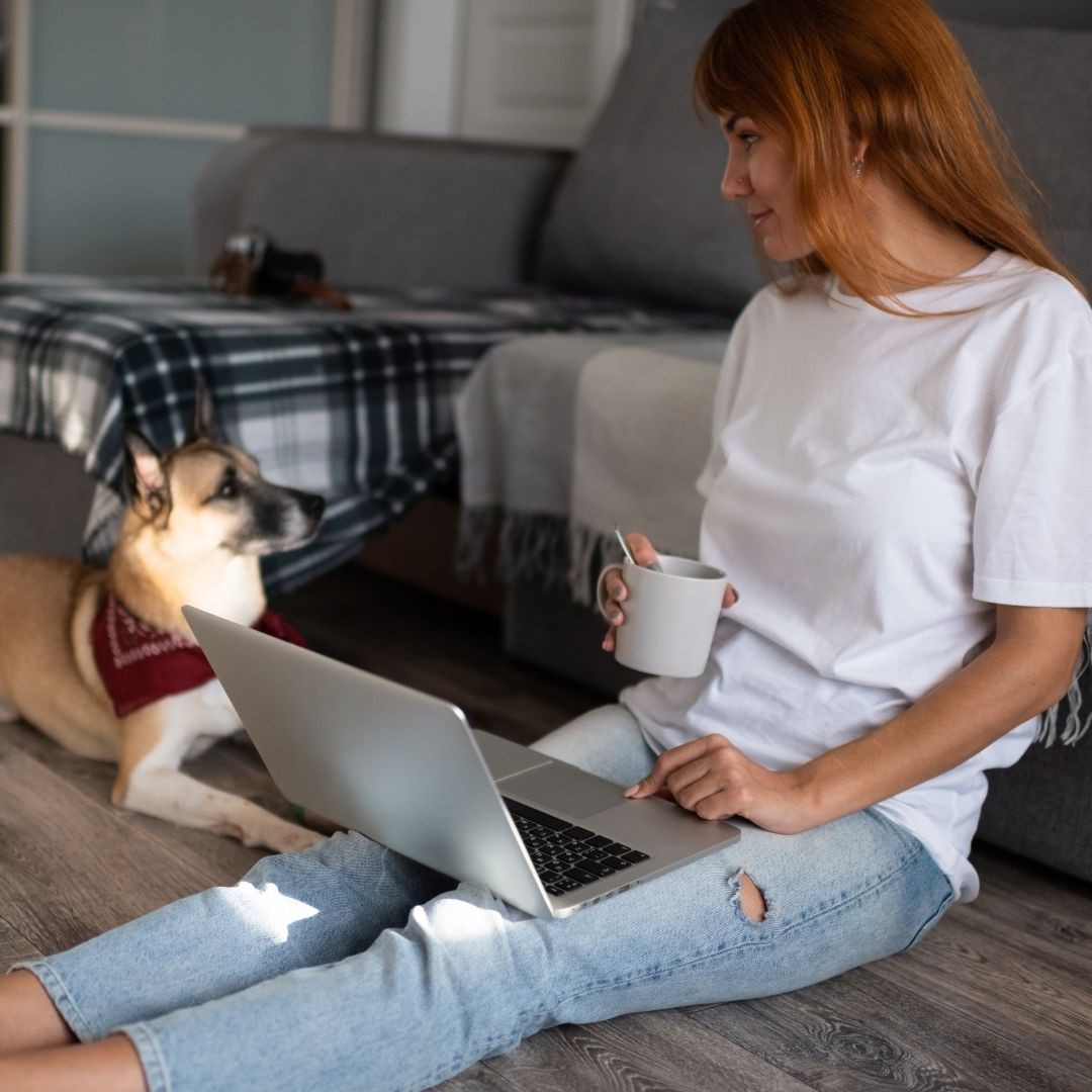 Dog sitting right next to a woman with laptop