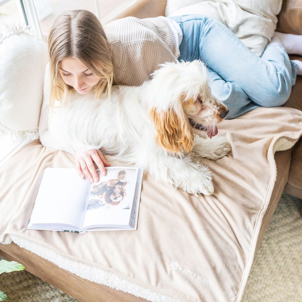 Woman and dog sitting on the couch and reading a book on the Potty Buddy blanket