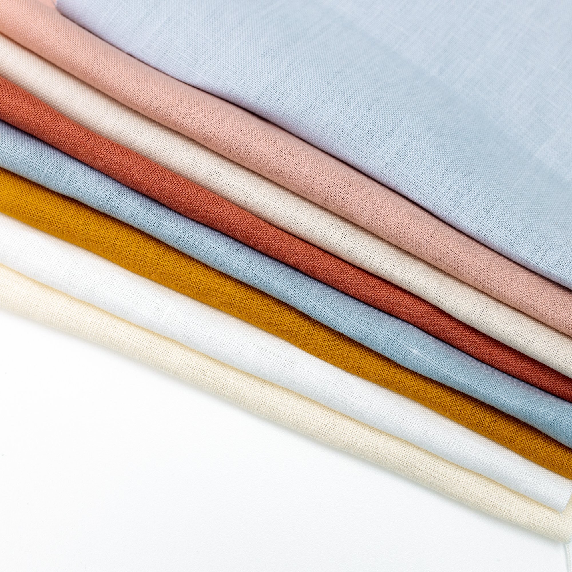 This image shows different coloured linens stacked on top of each other, available for purchase from the Clever Poppy Shop.