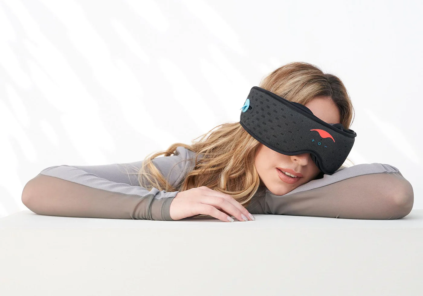 A blonde girl napping on her arms wearing a black Bluetooth sleep mask with headphones.