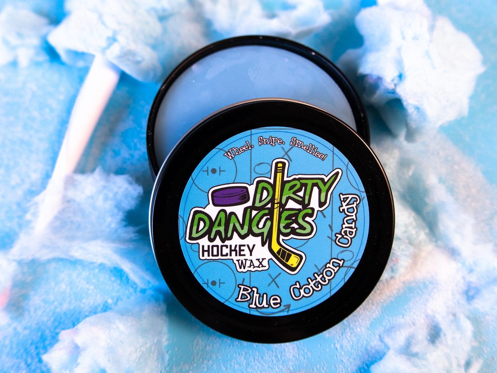 A tin of Dirty Dangles Hockey Stick Wax Blue Cotton Candy Scent sits open on a blue background surrounded by blue cotton candy.