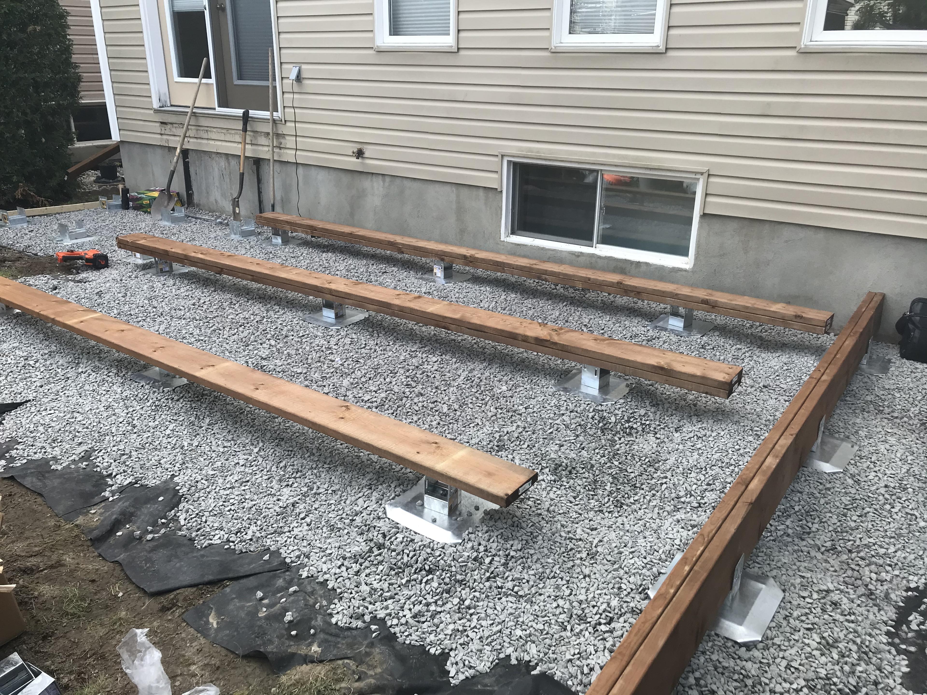 crushed stone layer with deck foot anchors installed in the ground showing the initial footing set up