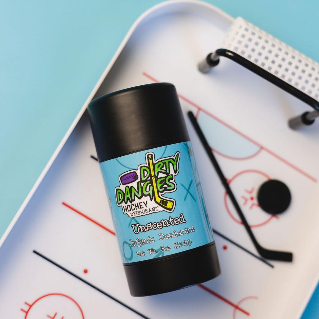 A tube of dirty dangles fragrance free aluminum-free unscented natural hockey deodorant on a blue background with hockey toys