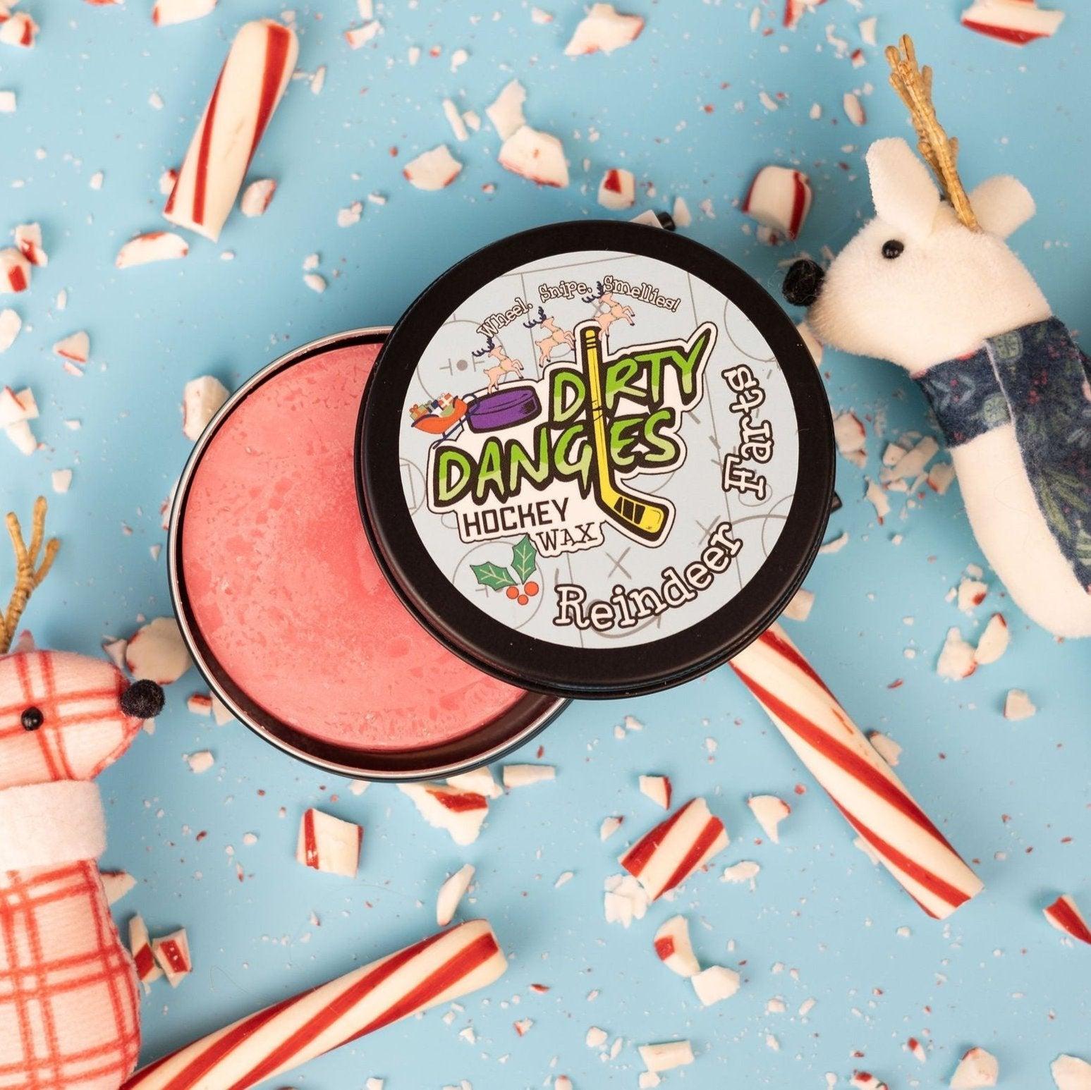 A tin of dirty dangles reindeer farts holiday hockey stick wax on a blue background with candy canes and reindeer