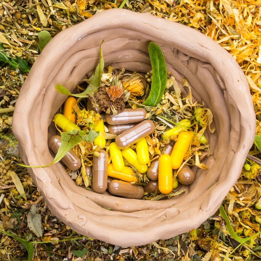 Rough ceramic bowl with herbal capsules and flower petals, surrounded by flower petals