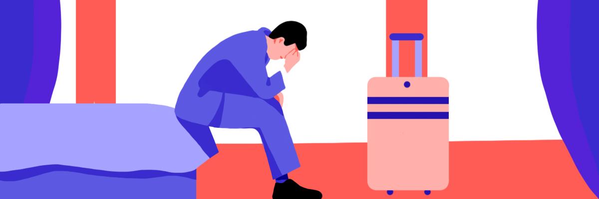 A stressed male sitting down on a bed leaning his elbow on his suitcase handle.
