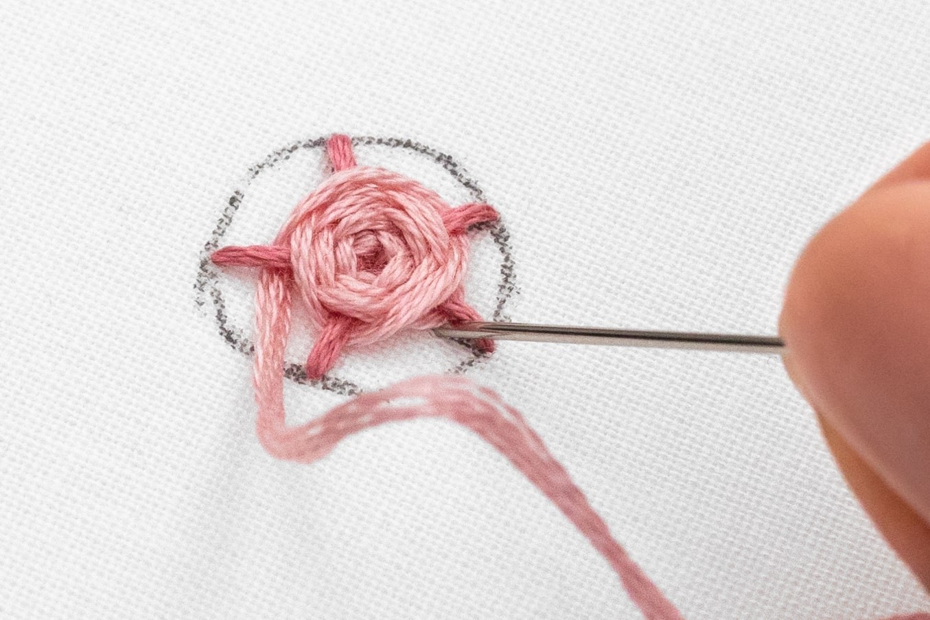 A needle is brought under a spoke of a woven rose.