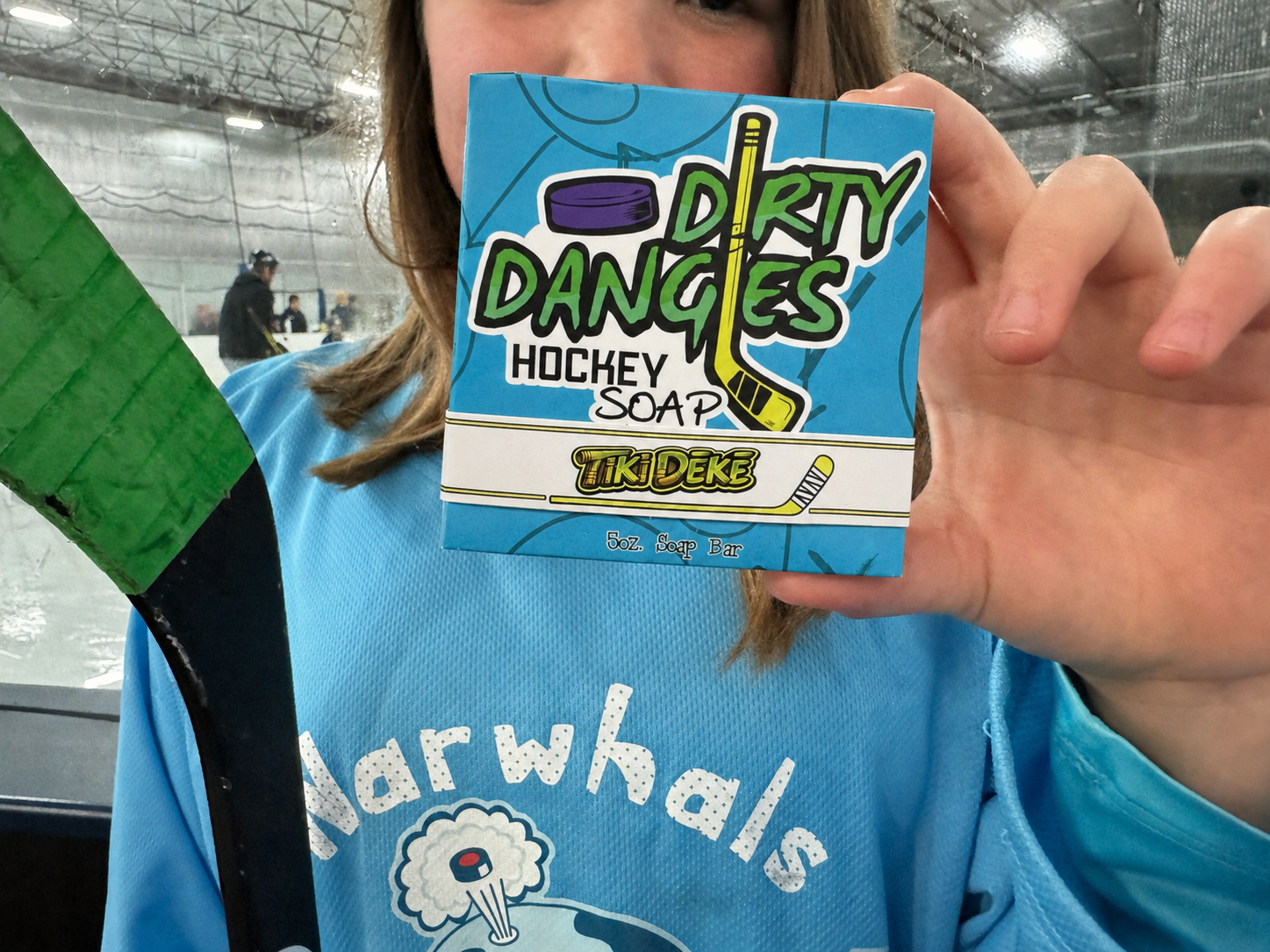 A girl hockey player holding a bar of tiki deke tropical coconut hockey soap inside an ice rink