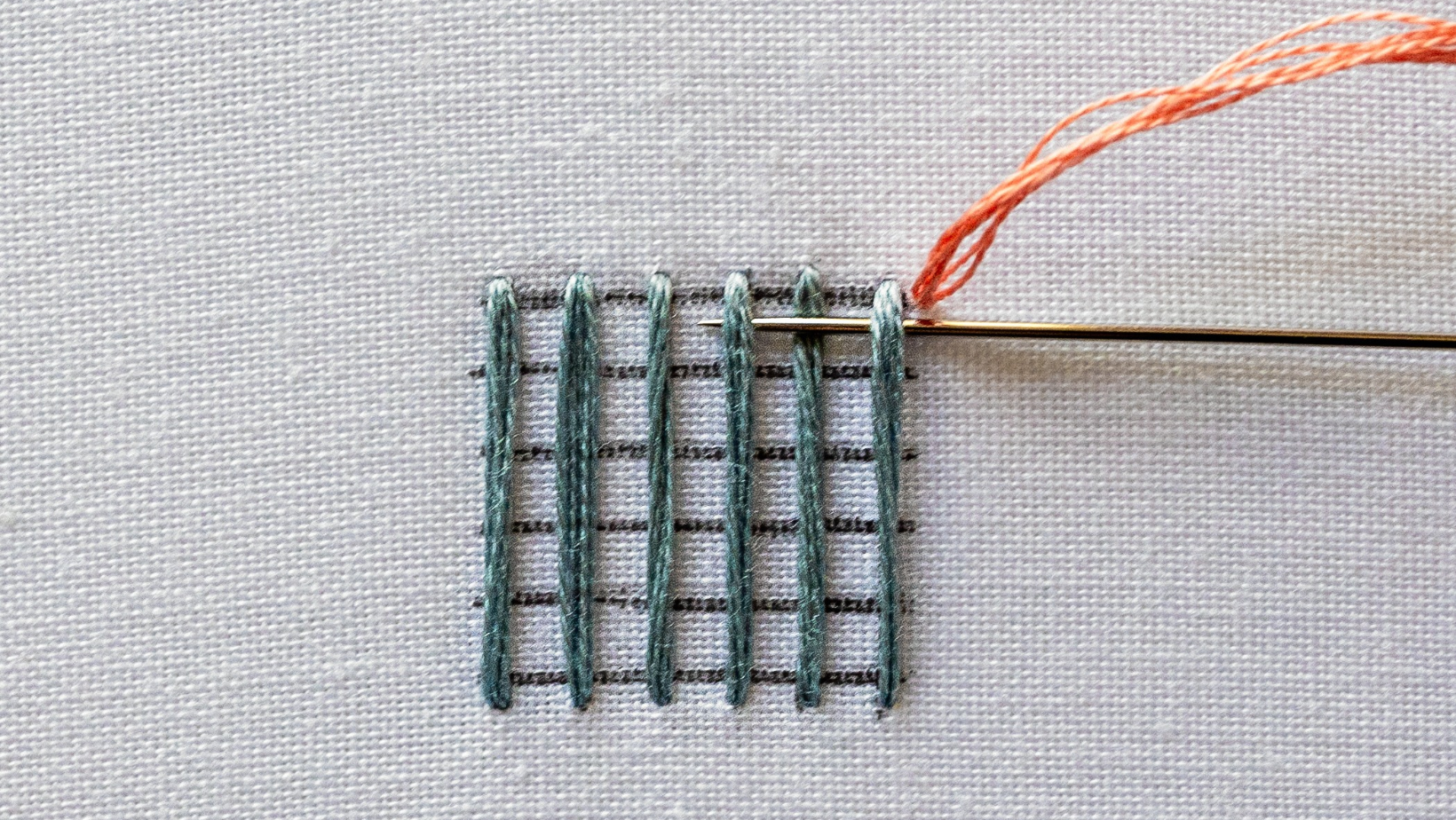 A needle passing under one warp thread and over the next, staying on the fabric surface
