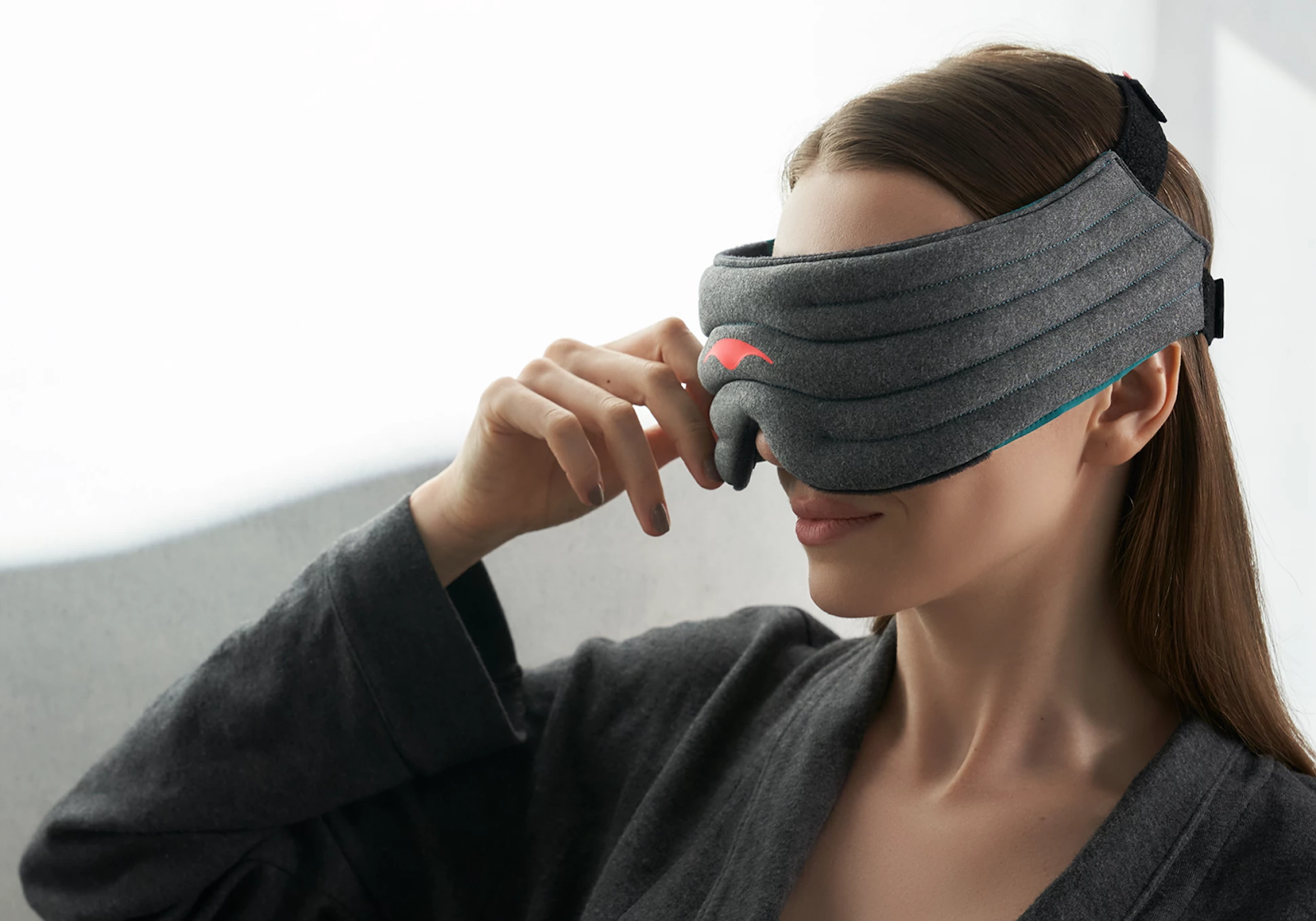 A girl touching the edge of the therapeutic sleep mask with a weighted head strap and eye cups around her head.