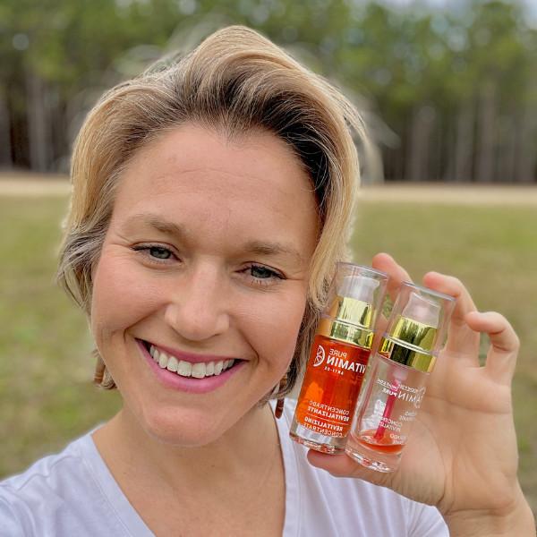 Mature woman smiling as she holds up two Vitamin C Serums, one empty, one full.