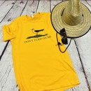 Picture of a gold and yellow t shirt with a picture of a seagull standing in the grass. Text on the shirt says "Don't Turd On Me." Similar to the Gadsden "Dont Tread On Me" Flag