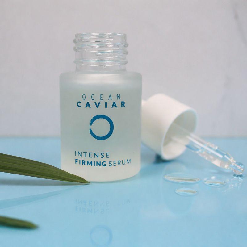 Caviar Firming Oil with its lid off sitting next to the bottle on a half blue, half gray background