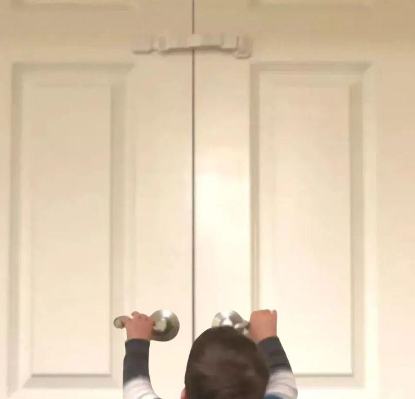 a toddler trying to open the door but he cant as there is a door buddy door strap