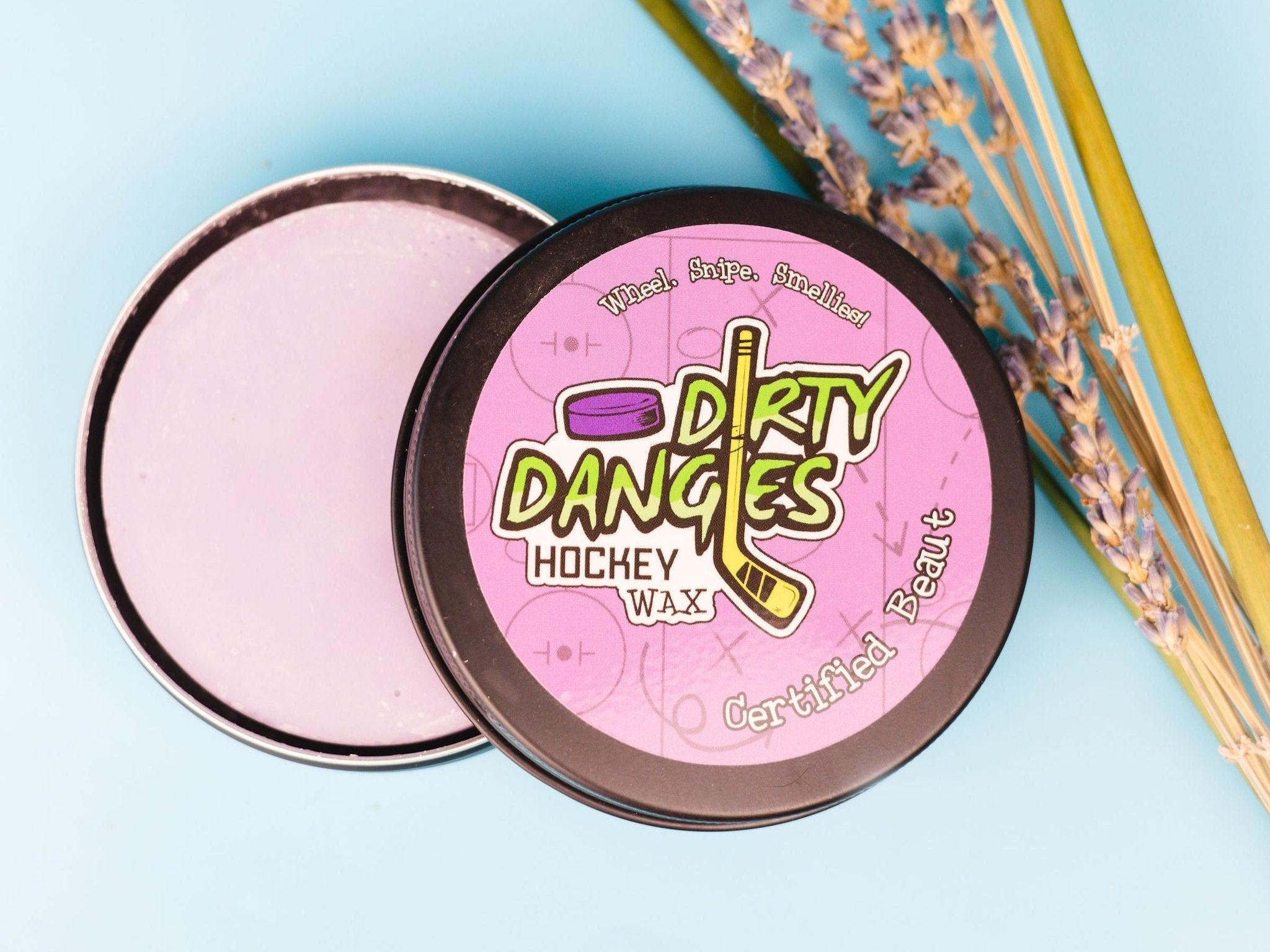 A tin of dirty dangles girls and womens hockey stick wax on a blue background with lavender and lemongrass