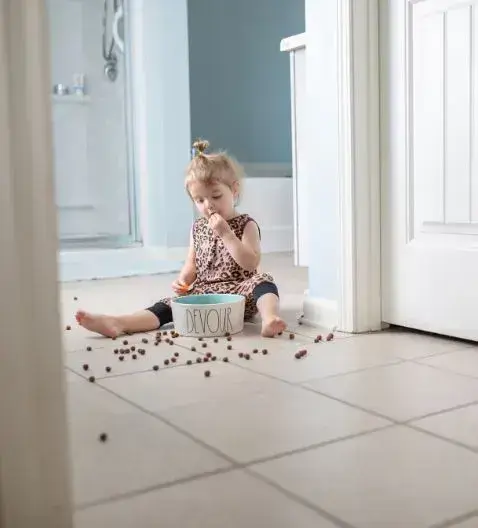 A little girl sitting on the floor, happily eating a handful of dog food
