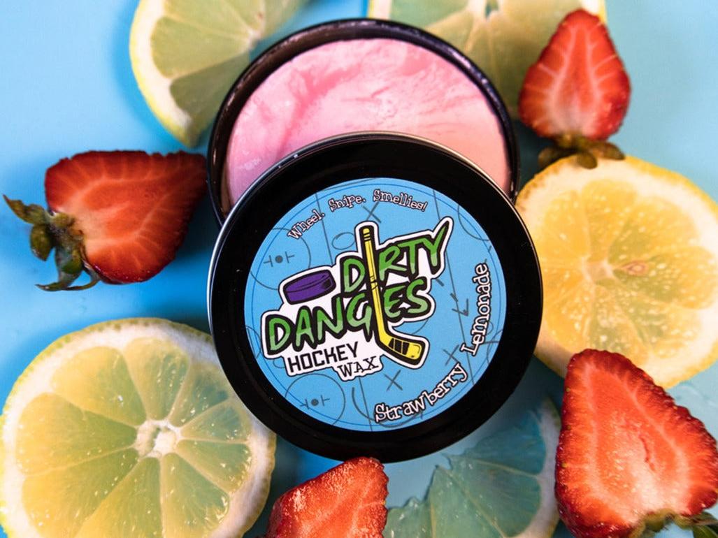 A tin of Dirty Dangles Hockey Stick Wax Strawberry Lemonade Scent sits open on a blue background surrounded by Strawberries and lemons