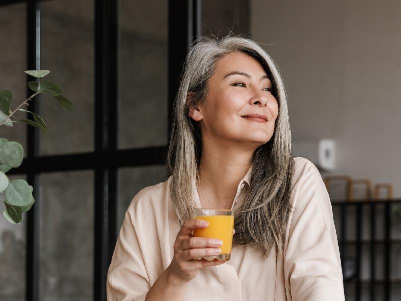Person smiling in the kitchen and holding a glass of orange juice.
